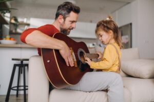 Father showing his daughter how to play the guitar