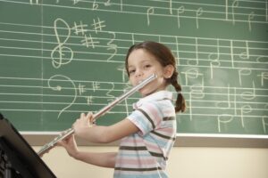 Little girl standing in front of a chalk board playing the flute