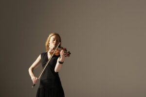Red haired woman in a black dress playing the violin