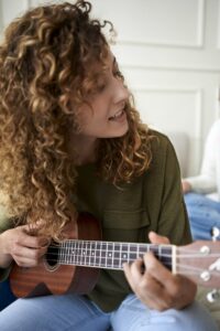 Curly haired woman sitting down playign the ukulele