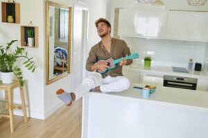 Young man sitting on a kitchen counter strumming a blue ukulele
