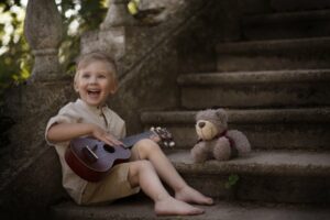 Little boy smiling sitting on some stairs holding a ukulele