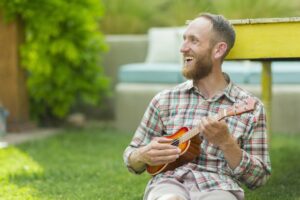 Man sitting outside smiling playing the ukulele