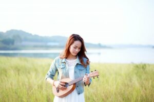 Woman standing in a field playing the ukulele