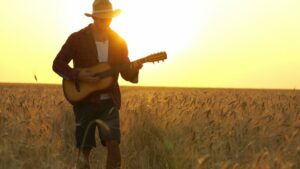 Man holding guitar in a wheat field