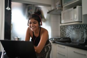 Young woman standing in her kitchen looking down at her laptop