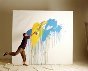 Young man throwing cans of paint on a large canvas