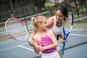 Woman showing little girl how to play tennis