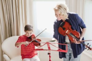 Little boy learning to play the violin with a female instructor