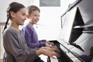 Brother and sister in purple shirts playing the piano