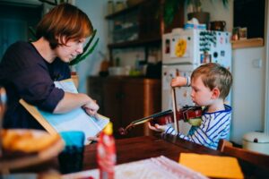 Little boy learning to play the violin at the kitchen table