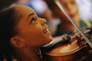Little girl looking up smiling while playing the violin