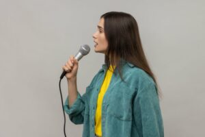 Woman standing in a green jacket singing into a microphone