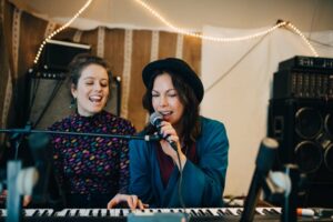 Two women singing along while playing piano