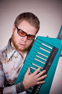 Man in glasses holding up a keytar