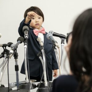 Little boy in a suit surrounded by microphones