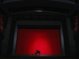 Picture of a grand piano on a stage with red curtains