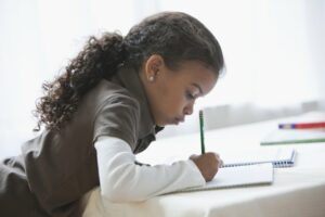 Little girl with curly hair writing on a paper