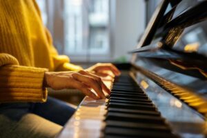 Close up of a woman in a yellow sweater playing the piano