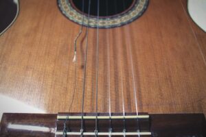Close up of a brown acoustic guitar with a broken string