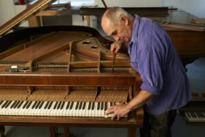 Older man in a purple shirt tuning a piano