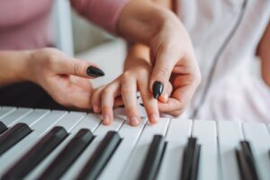 Woman helping child with finger placement on piano