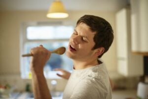 Young man singing into a wooden spoon in his kitchen