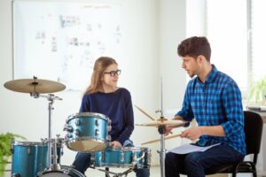 Male teacher showing girl how to play drums