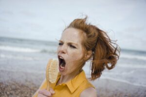 Young red haired woman singing into a hairbrush at the beach