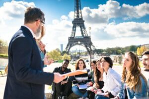 Male professor teaching a lesson outside to a group of students with the Eiffel tower in the background