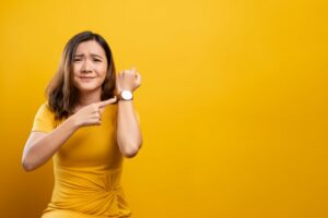 Woman pointing to her watch in front of a yellow background