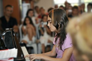 Close up of a little girl playing the piano in front of a group of people