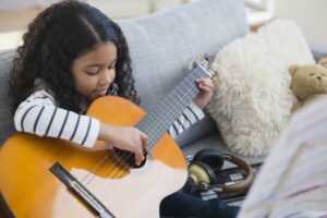 Little girl sitting on her ocuch holding an acoustic guitar