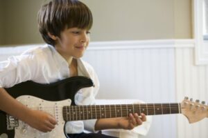 Little boy in a white shirt holding a black electric guitar