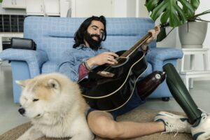 Man playing guitar sitting on the floor next to his dog