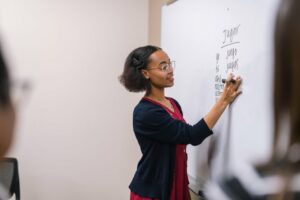 Young woman wearing glasses writing Spanish on a white board