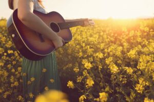 Woman holding guitar in a field of flowers