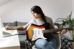 Young woman sitting at a desk taking guitar lesson notes online