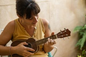 Woman in a yellow shirt looking down playing the ukulele