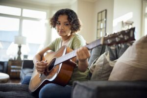 Teen girl playing the guitar in her living room