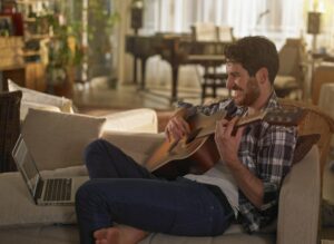 Man sitting back on his couch learning to play the guitar online 