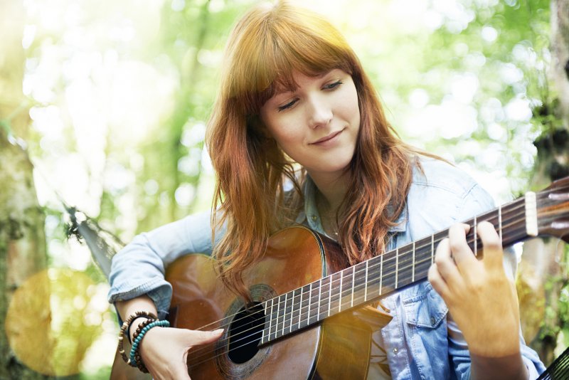 Young woman playing her guitar outside in a forest