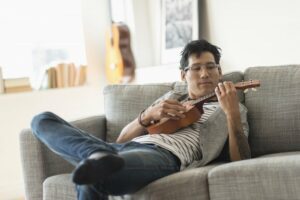 Young man wearing glasses playing the ukulele on the couch