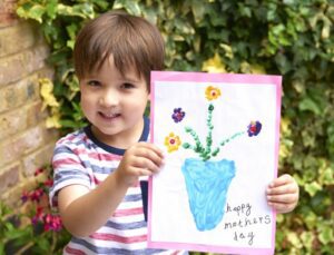 Little boy holding up a Mother's Day card