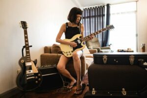 Woman sitting playing electric guitar surrounded by music equipment