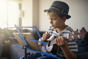 Little boy practicing ukulele with an online lesson