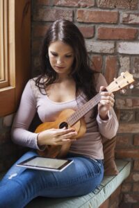 Young woman sitting down learning to play the ukulele