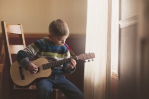 Little boy sitting on a chair playing the guitar