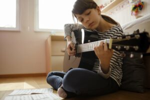 Pre teen girl sitting on the floor playing the guitar