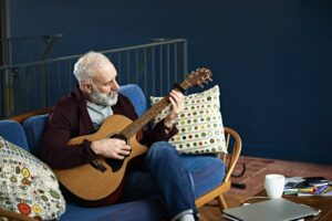 Older man playing the guitar on his couch